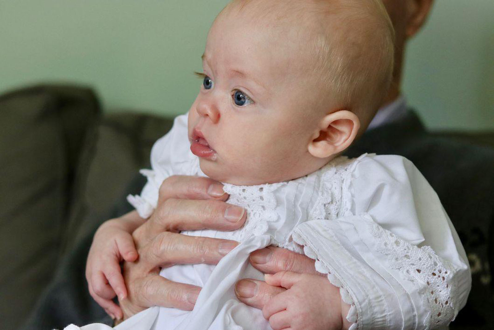 Baby in white dress being held up by hand around the body, waiting to take part in their Celebrant Naming Ceremony.